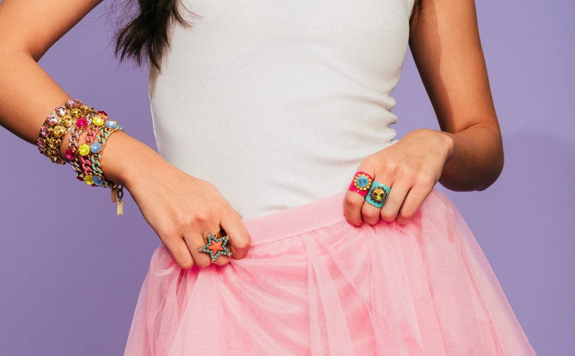 Person wearing colorful jewelry including rings and a bracelet on a purple background