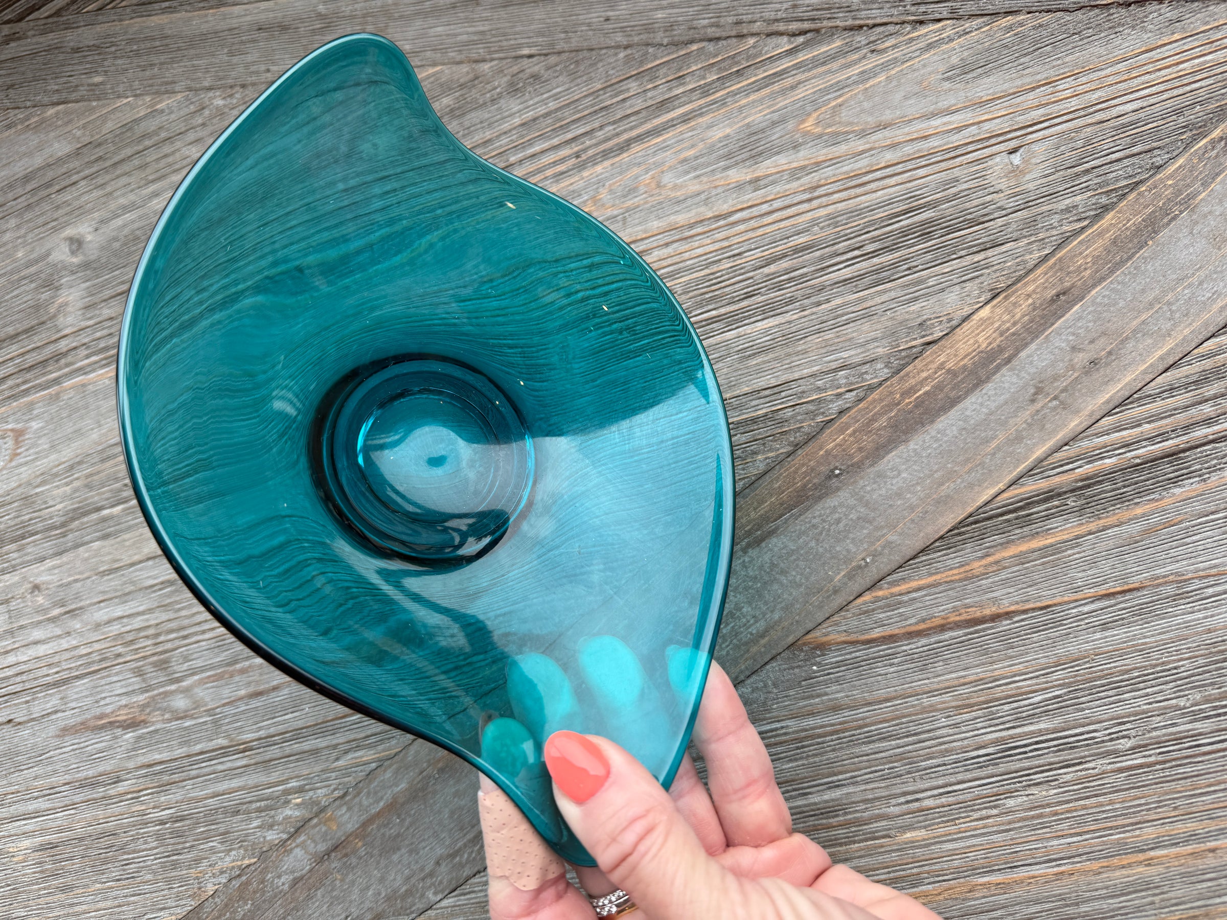 Teal glass bowl held by a hand on a wooden surface