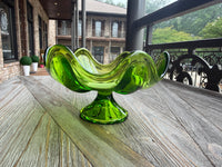 Green glass bowl on a wooden table with a building and trees in the background