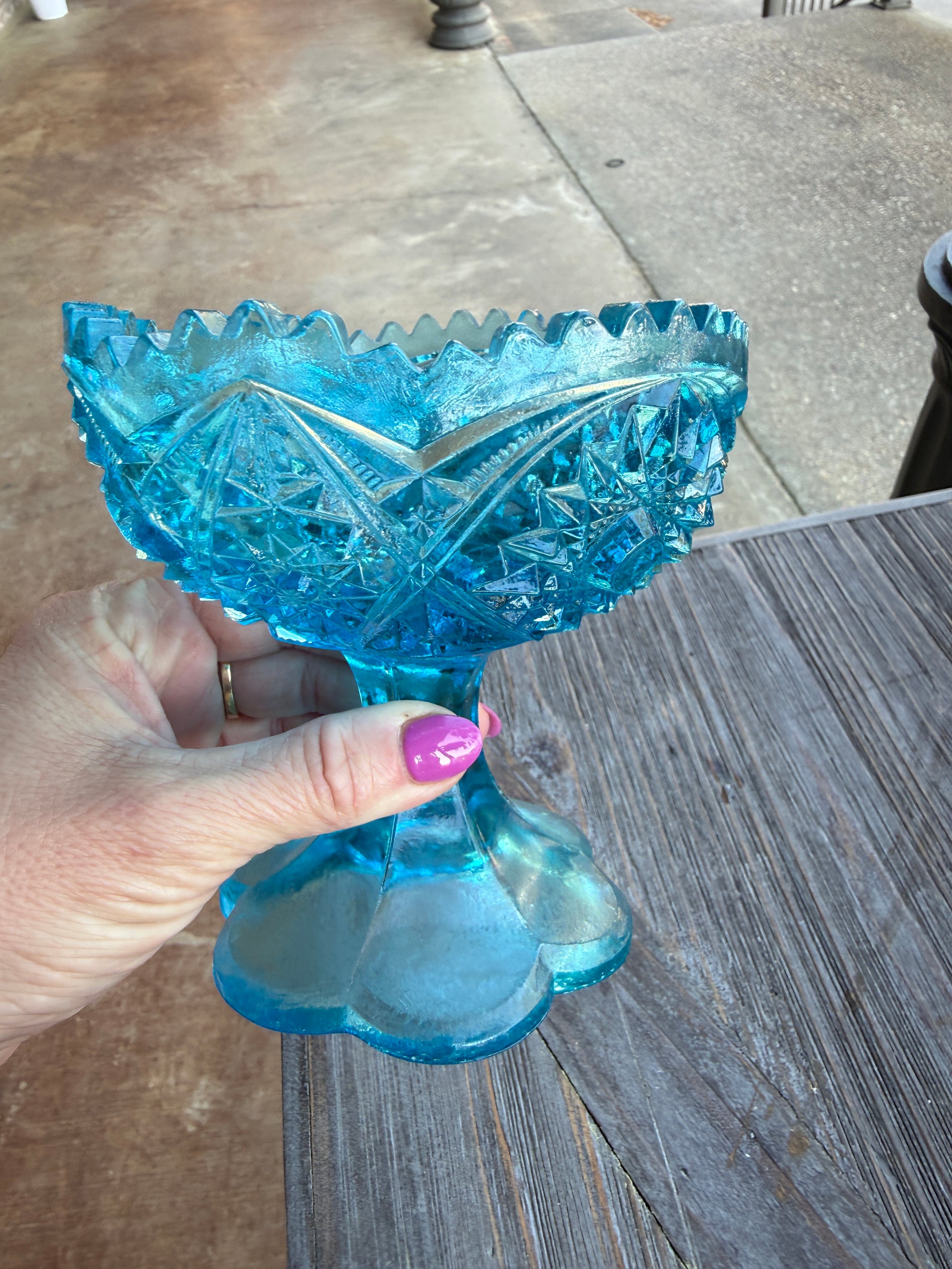 Hand holding a blue glass candy dish on a wooden surface
