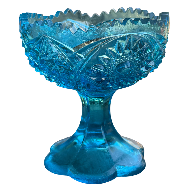 Blue glass footed bowl with intricate cut patterns on a white background