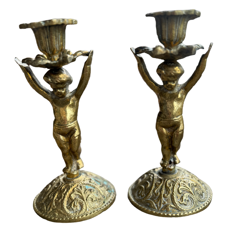 Pair of ornate brass candle holders with figurines holding bowls on a white background