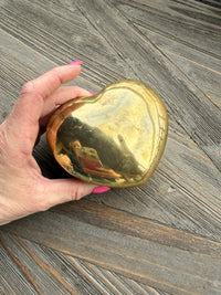 Hand holding a gold heart-shaped object on a wooden surface