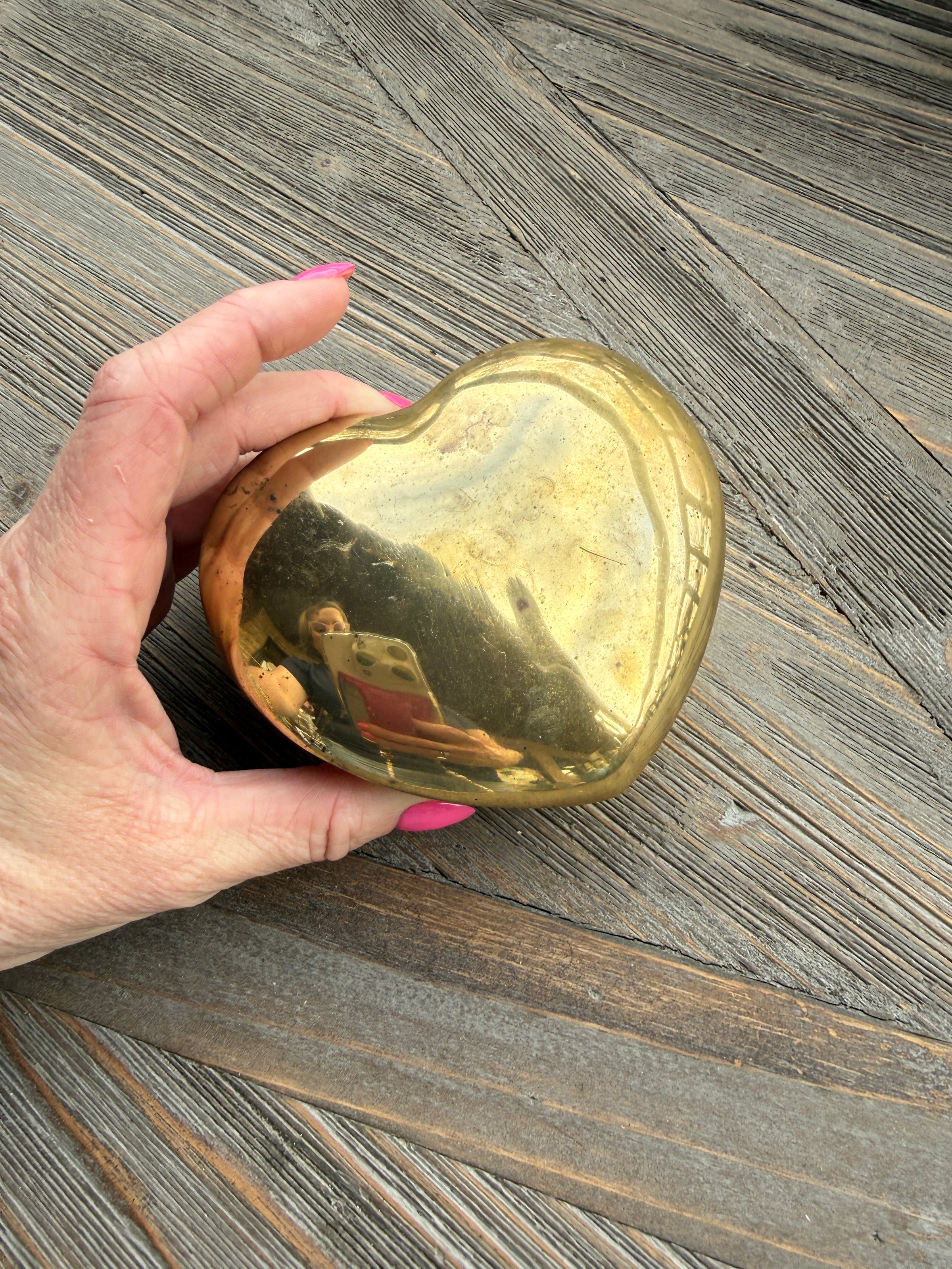Hand holding a gold heart-shaped object on a wooden surface