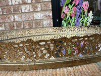 Decorative gold metal frame with floral design against a brick wall.