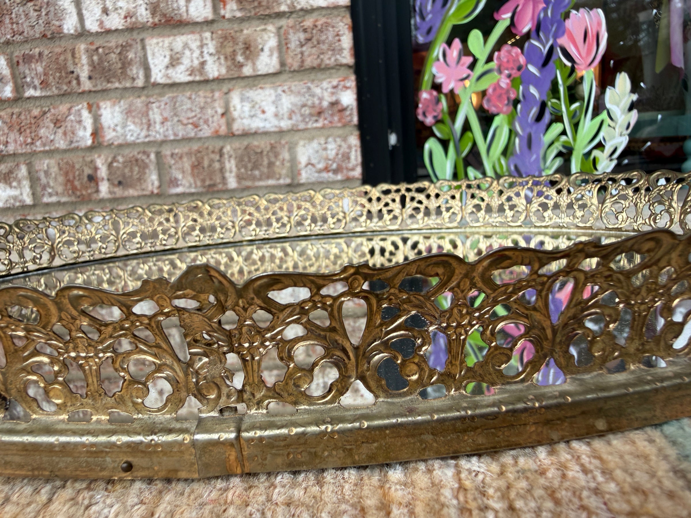 Decorative gold metal frame with floral design against a brick wall.