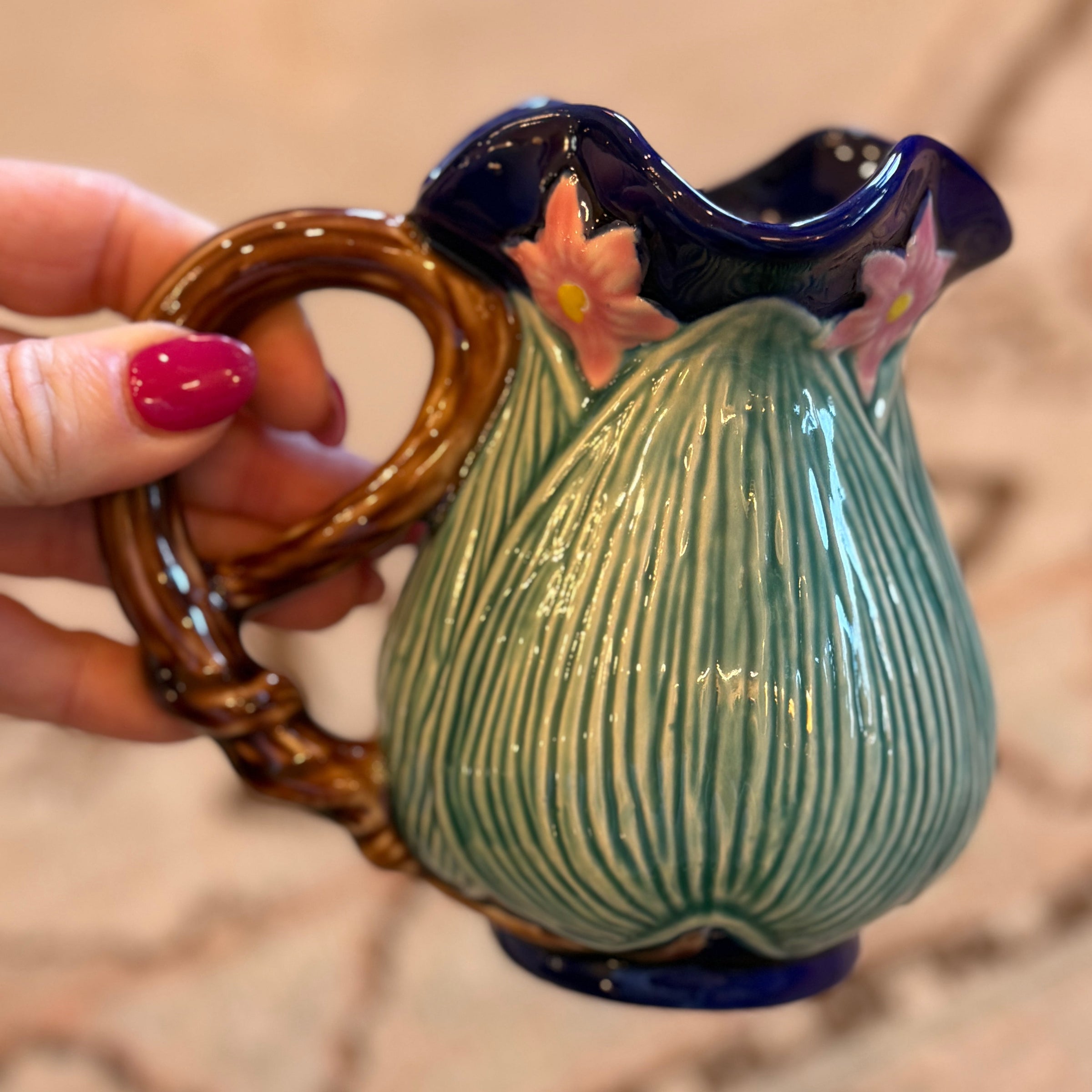Ceramic pitcher with decorative handle held by a hand on a textured surface