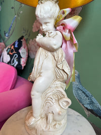 Decorative statue of a cherub with a pink bow on a table against a colorful background