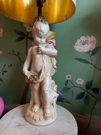 Statue of a child holding a flower against a floral wallpapered wall.