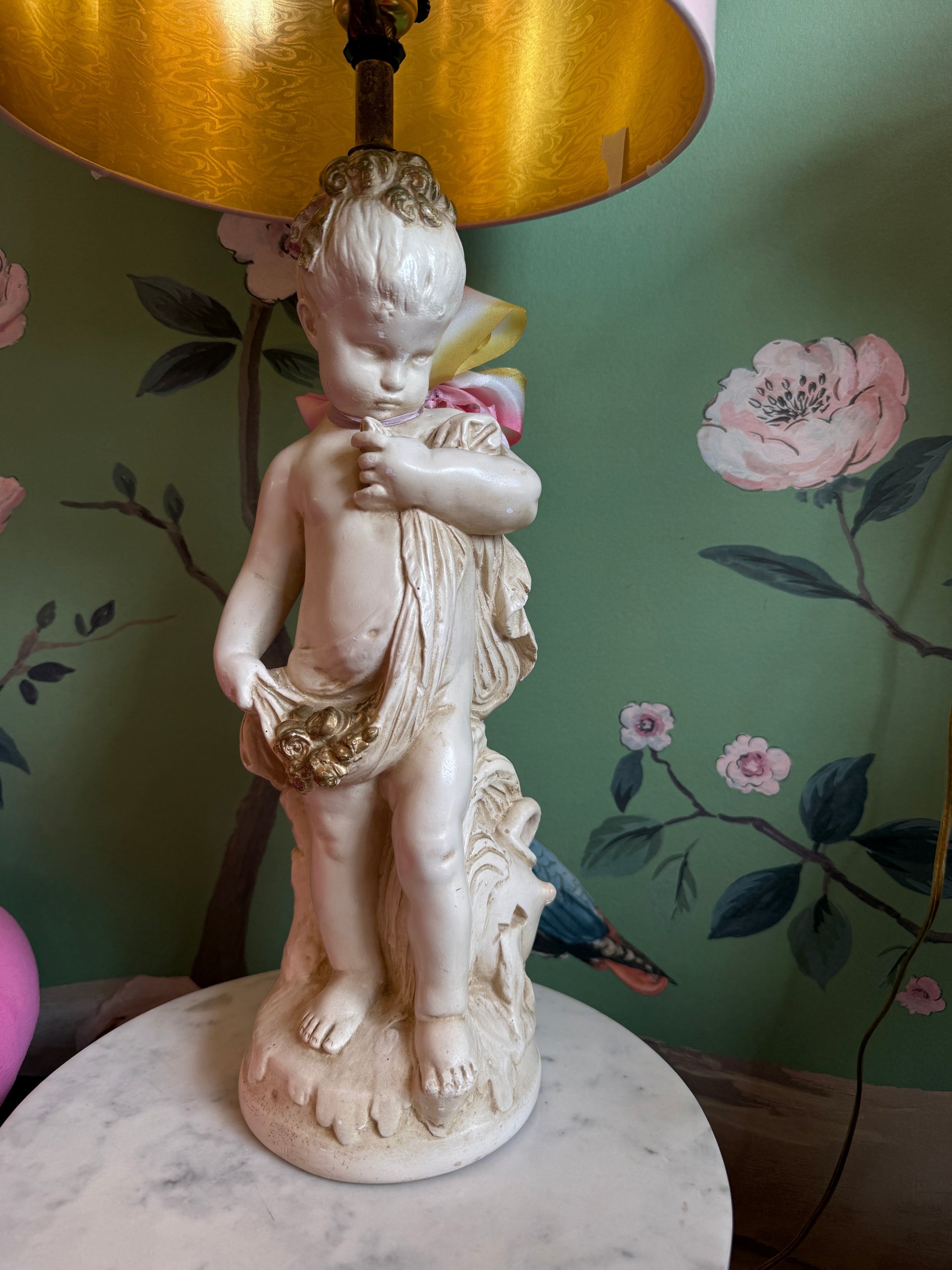 Statue of a child holding a flower against a floral wallpapered wall.