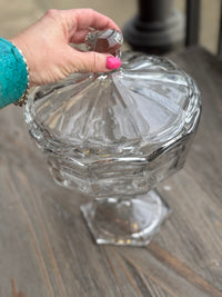 Clear glass candy dish held by a hand with pink nail polish on a wooden surface