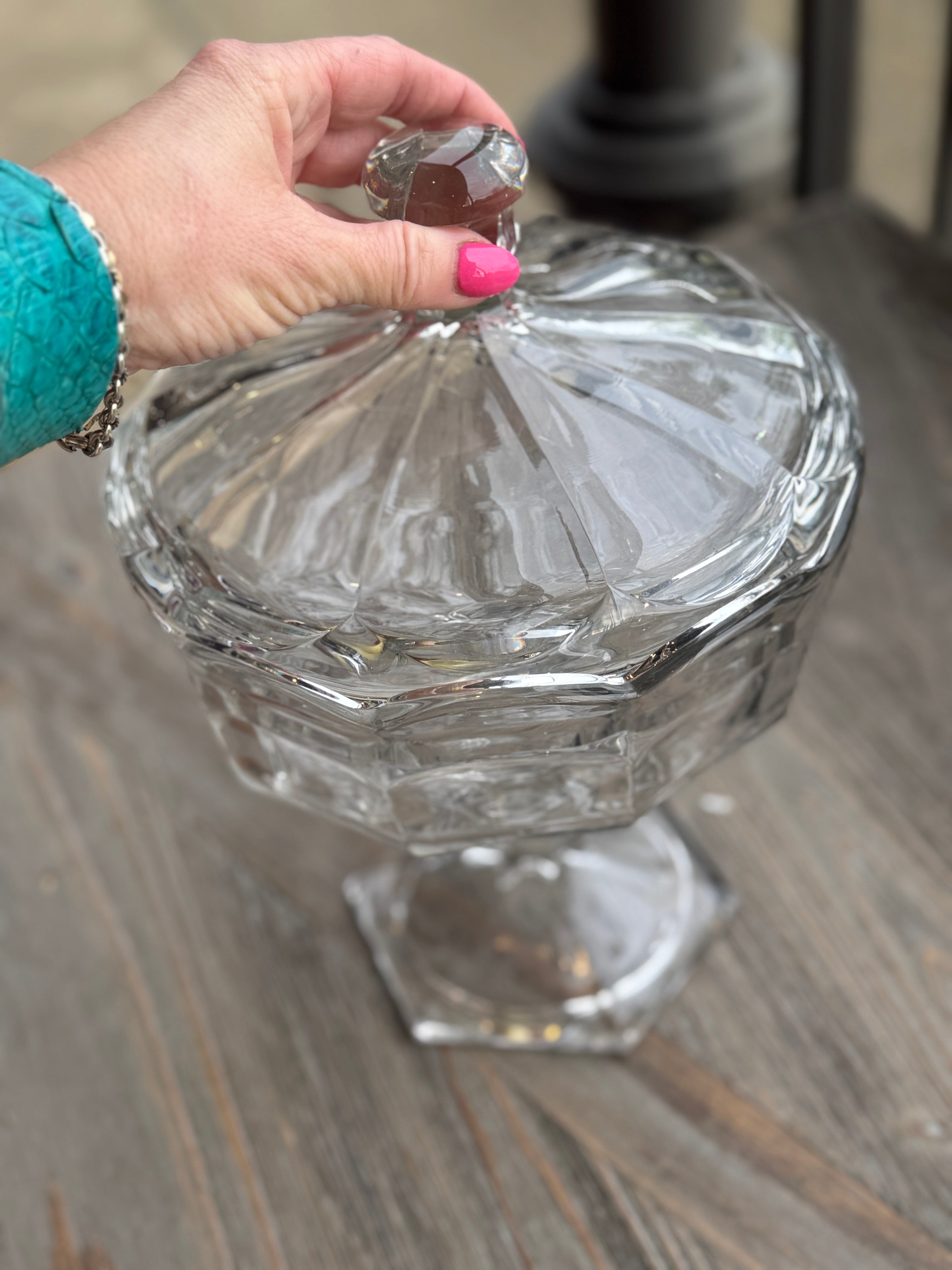 Clear glass candy dish held by a hand with pink nail polish on a wooden surface
