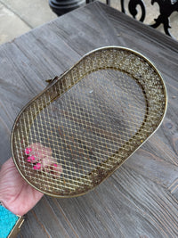 Gold mesh strainer held by a hand on a wooden surface