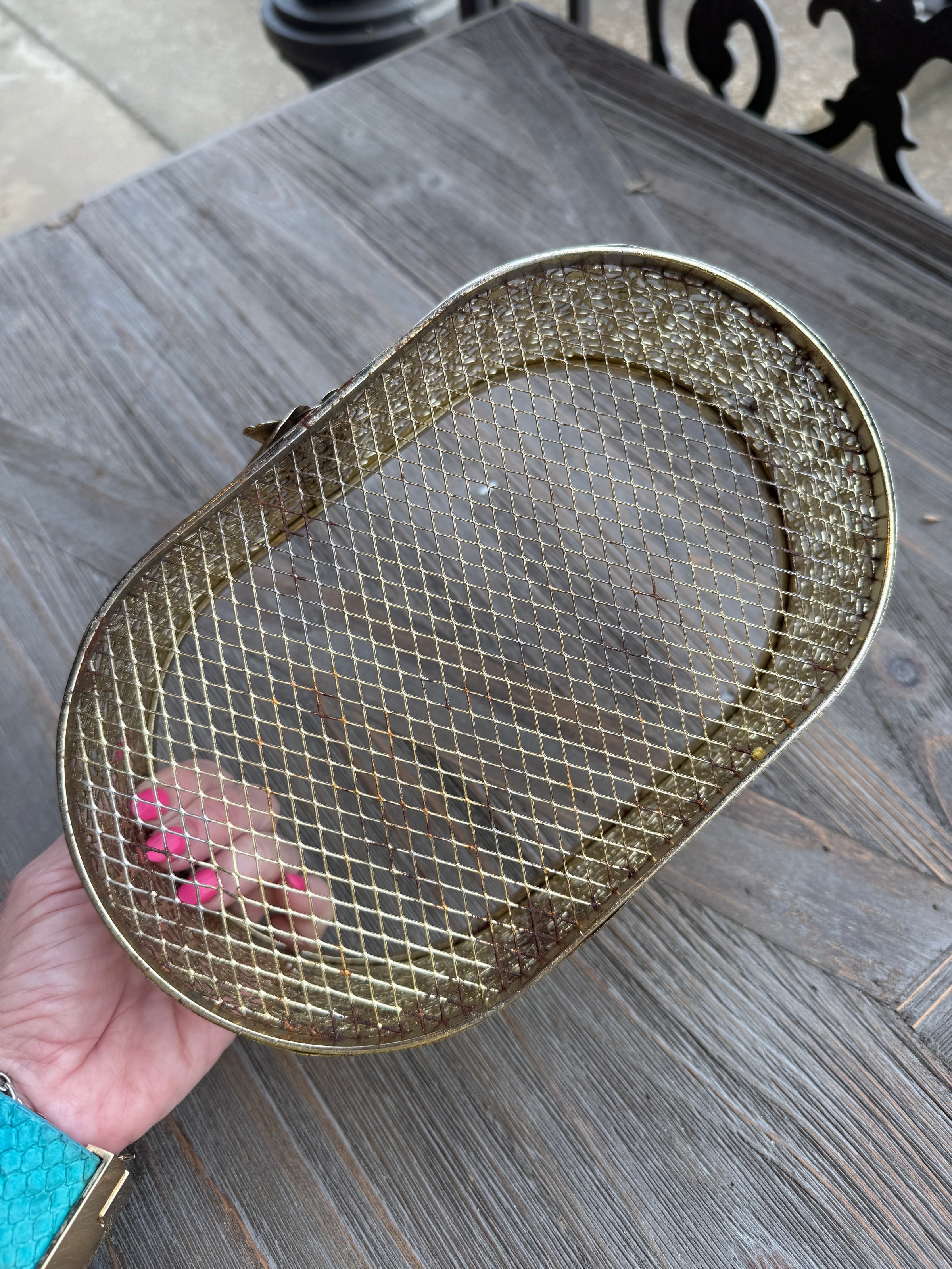 Gold mesh strainer held by a hand on a wooden surface
