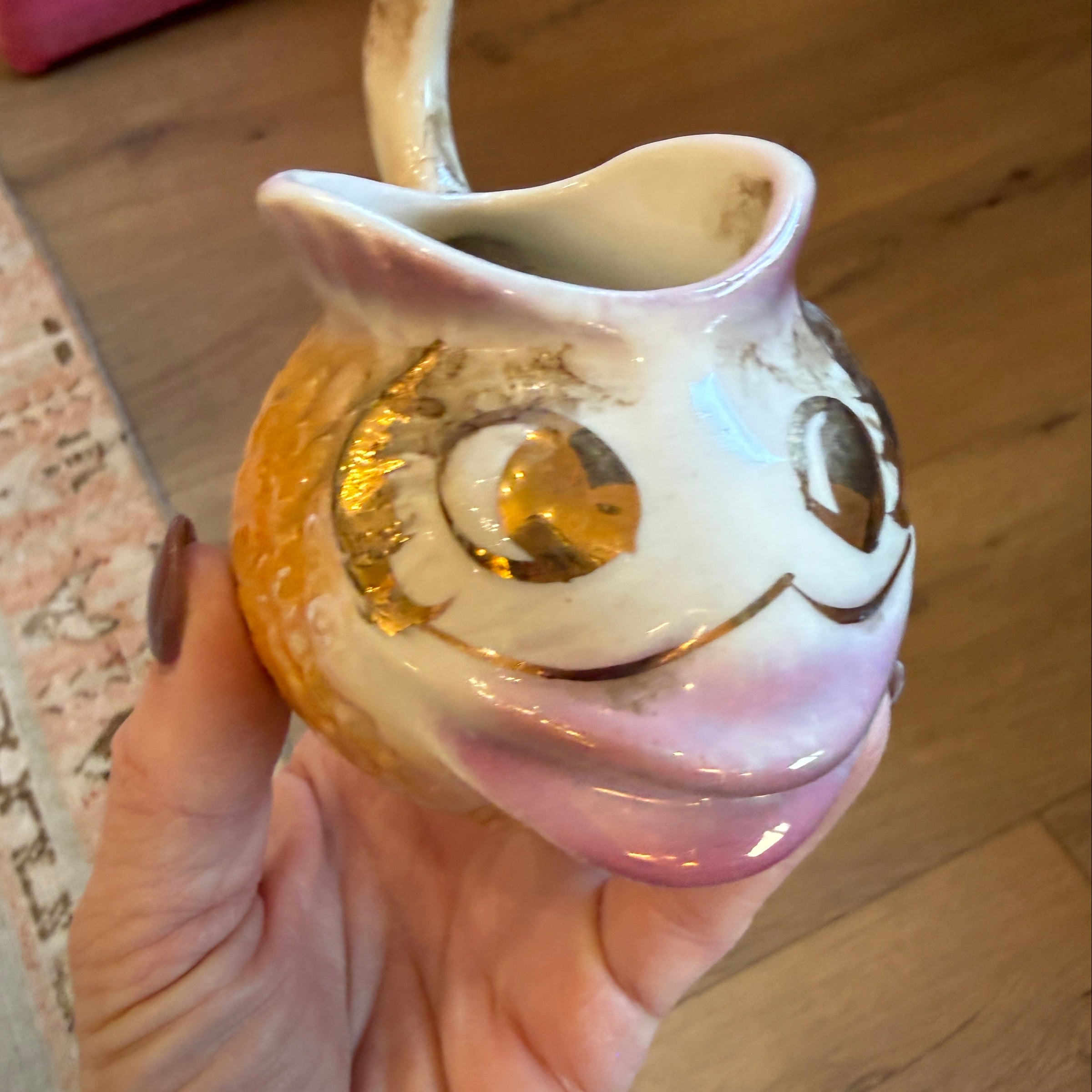 Hand holding a decorative shell with gold interior on a wooden floor.
