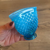 Blue textured object held by a hand against a wooden background