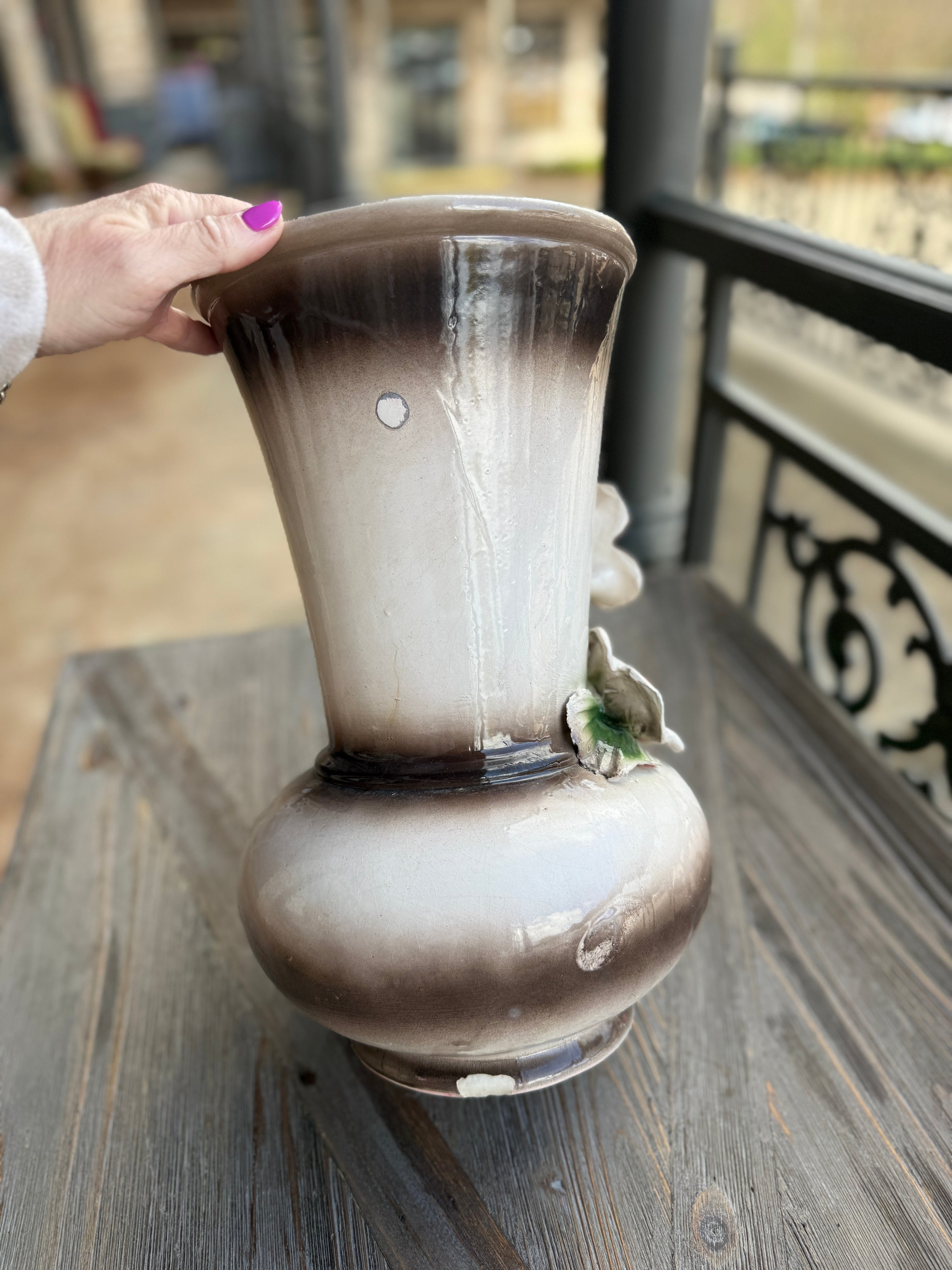 Person holding a decorative vase on a wooden surface with a blurred background