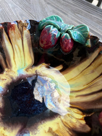 Close-up of a ceramic piece with leaf and berry design on a textured surface