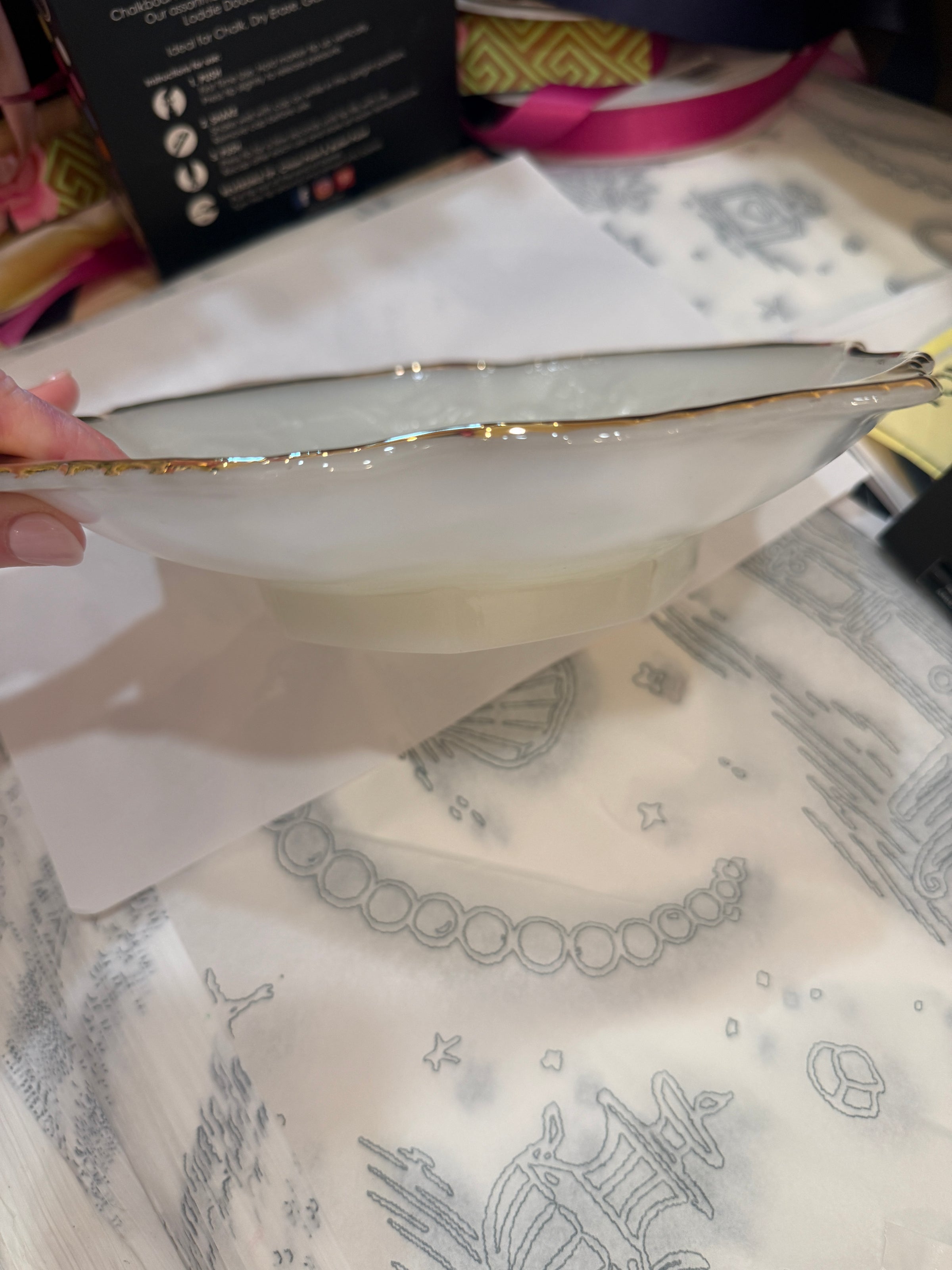 White ceramic plate with gold rim held over a patterned fabric background