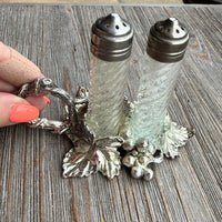Decorative salt and pepper shakers on a wooden surface with a hand holding the holder.