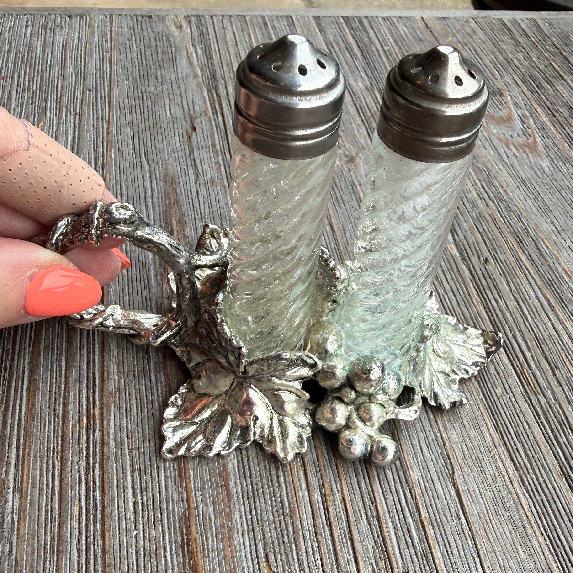 Decorative salt and pepper shakers on a wooden surface with a hand holding the holder.