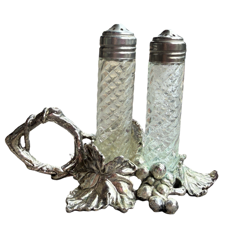 Decorative salt and pepper shakers with a silver holder on a white background