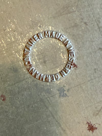 Circular metal stamp with 'Made in Western Germany' text on a textured surface