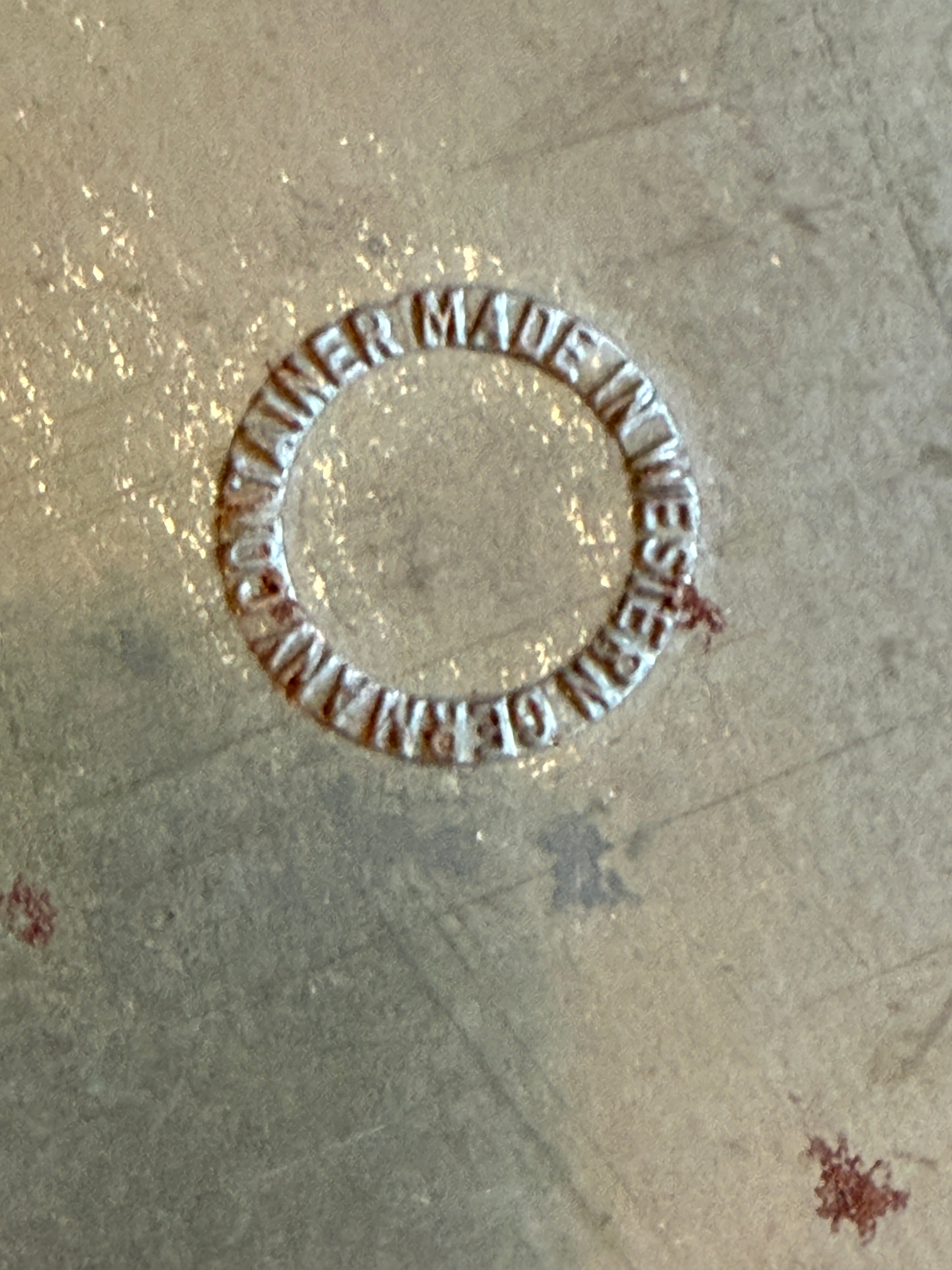 Circular metal stamp with 'Made in Western Germany' text on a textured surface