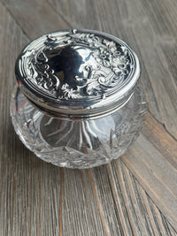 Decorative glass container with silver lid on a wooden surface