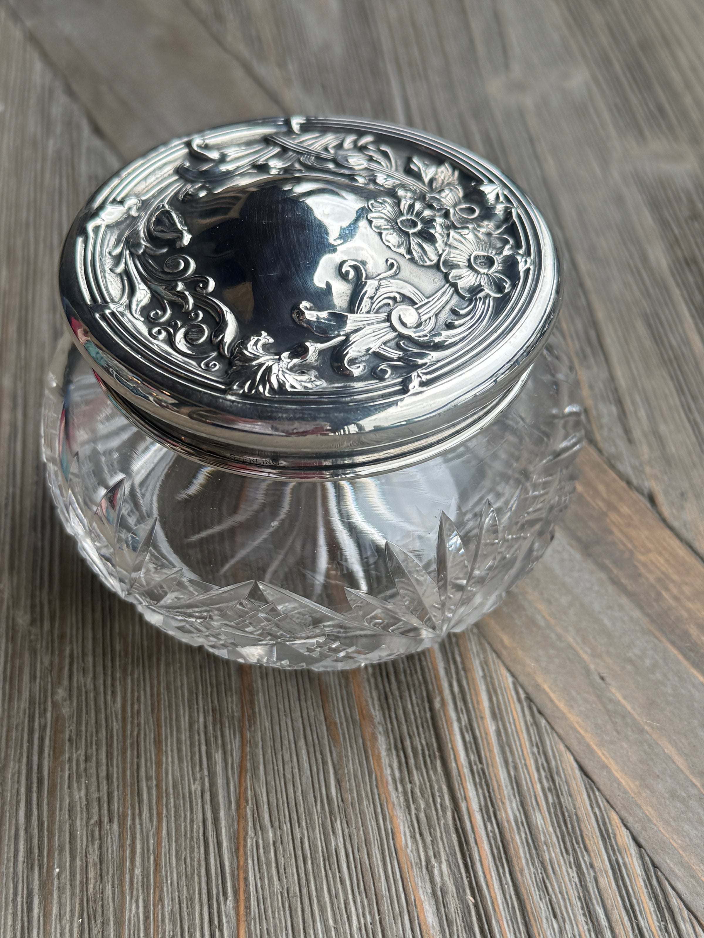 Decorative glass container with silver lid on a wooden surface