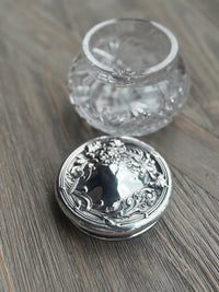 Silver decorative container lid and clear glass jar on a wooden surface