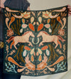 Person holding a dark green fabric with pink unicorn and nature-themed patterns.