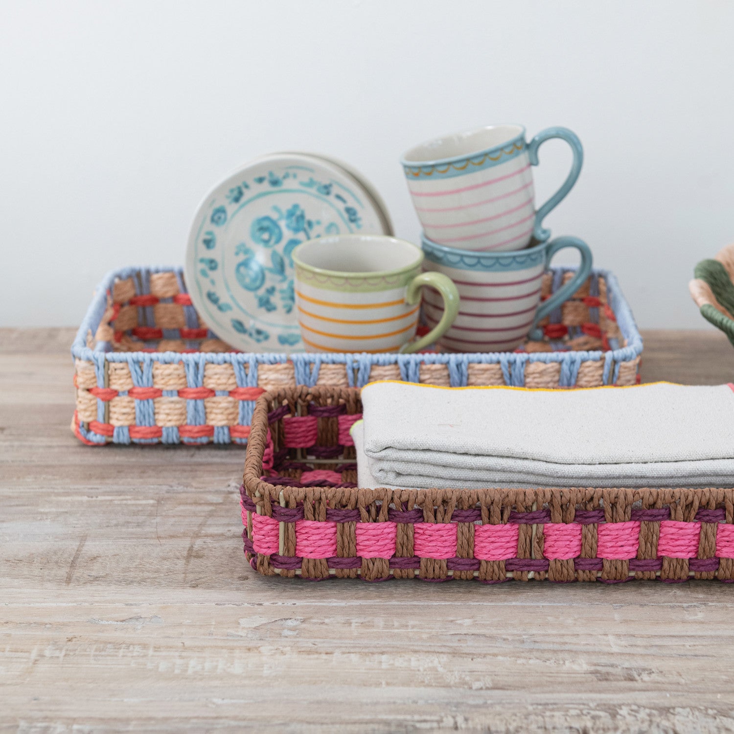 Colorful woven trays with cups and plates on a wooden surface